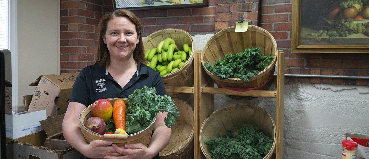 A woman holding a basket of vegetables, in front of a shelf displaying more food.